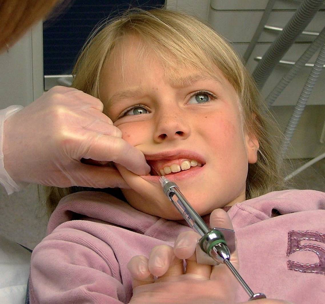 Photo of dentist making anesthetic injection to child&rsquo;s gum before extracting tooth.