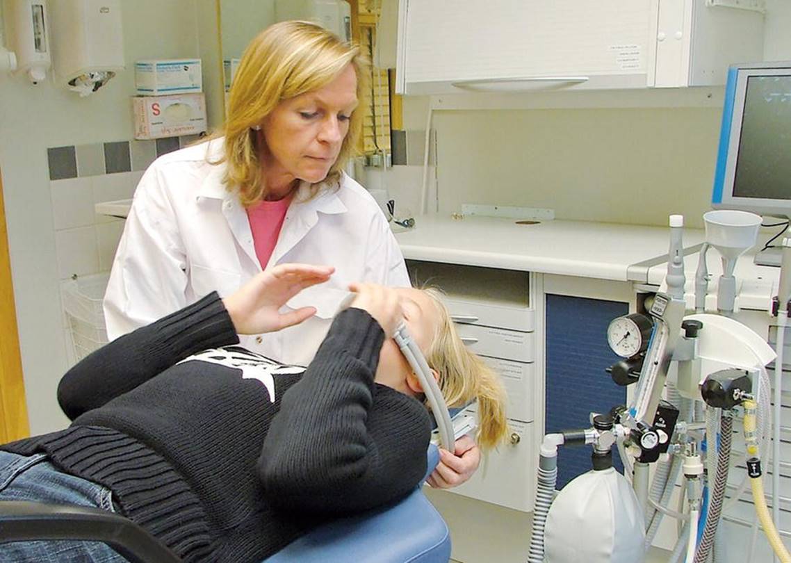 Photo displaying a dentist inserting water suction hose to the mouth of a girl for dental treatment.