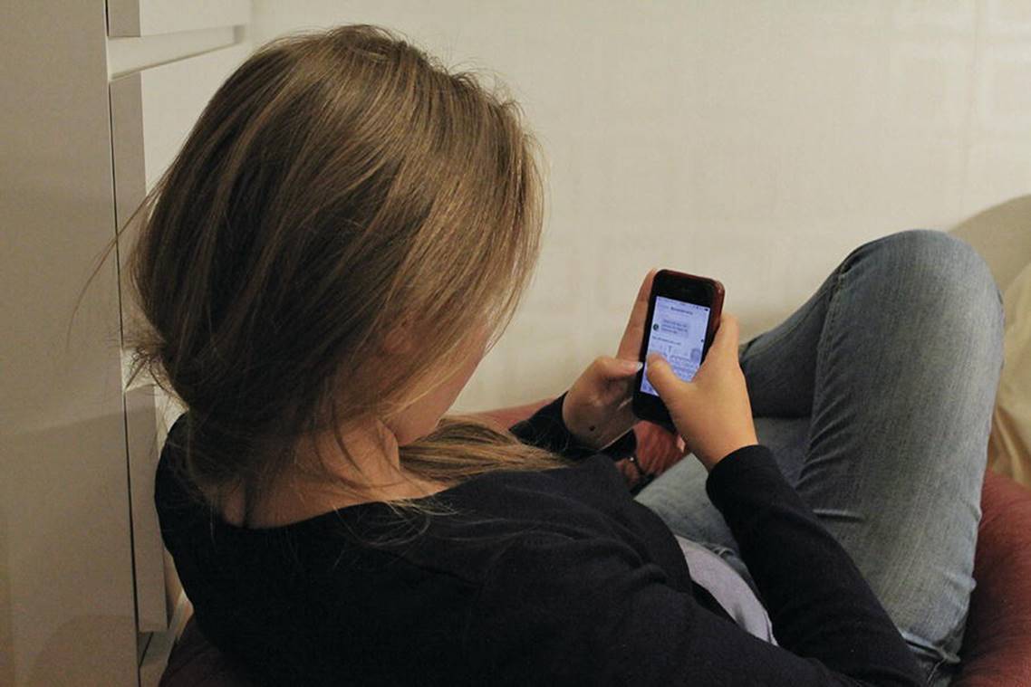 Photo displaying rear view of a girl slouchingly sitting, with leg crossed while texting.